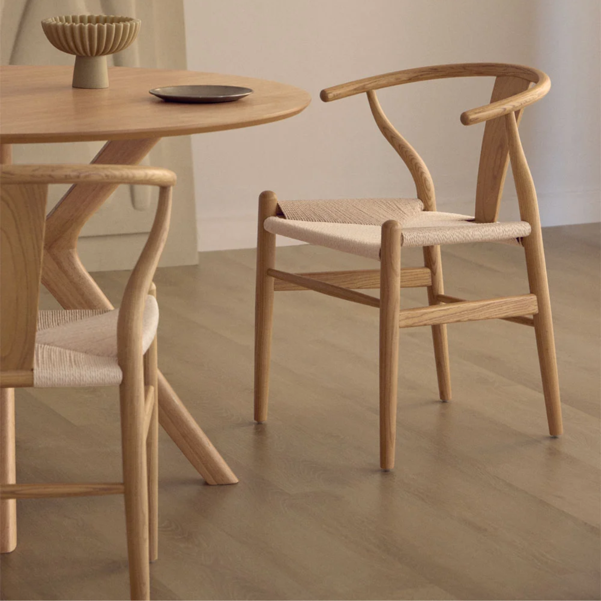 Sillas Wishbone de madera natural con asiento de cuerda junto a una mesa redonda